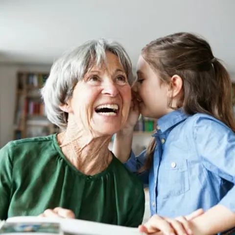 Mädchen flüstert Großmutter etwas ins Ohr